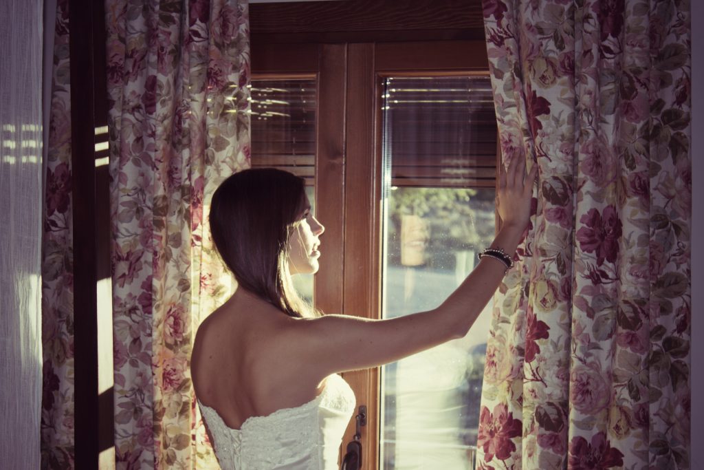 Chica vestida de novia abriendo las cortinas de una habitación de hotel